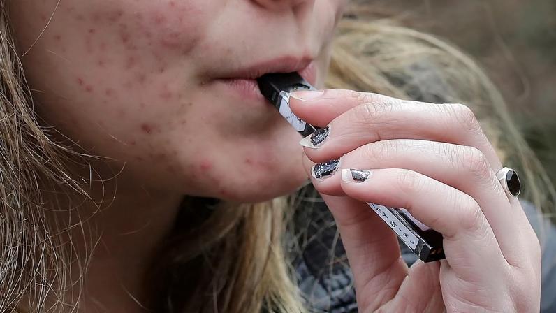 ARQUIVO - Um aluno do ensino secundário usa um cigarro eletrónico junto a um campus escolar em Cambridge, Massachusetts, em 11 de abril de 2018.