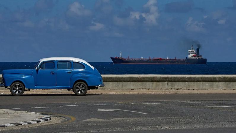 Um carro clássico americano circula no passeio marítimo enquanto um camião-cisterna sai de Havana, Cuba,