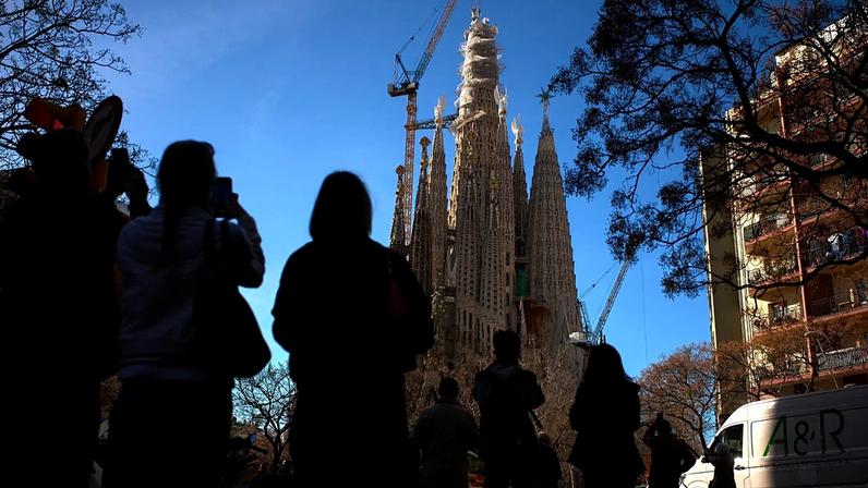 As pessoas observam enquanto uma grua eleva o braço superior da cruz para a Torre de Jesus Cristo na Sagrada Família em Barcelona, Espanha, na sexta-feira, 20 de fevereiro de 2026.