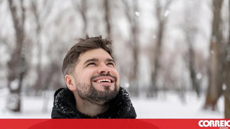 Homem sorri na neve; essenciais para o frio em destaque