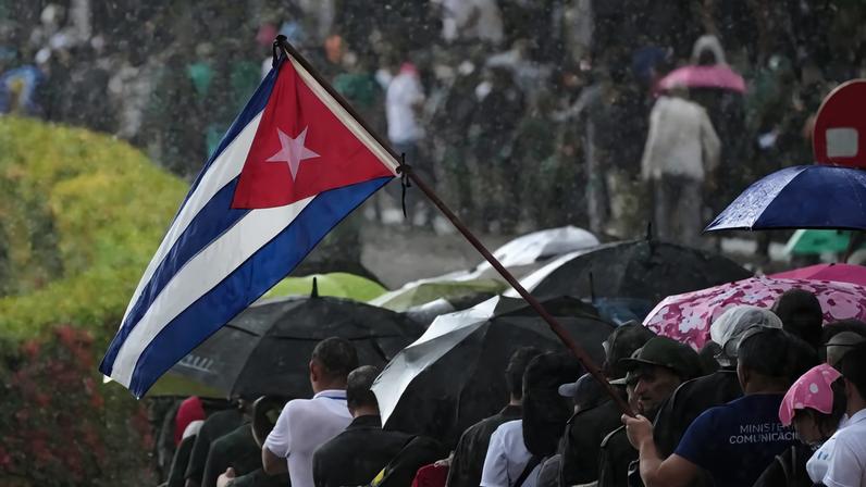 Militares cubanos em evento sob chuva com a bandeira de Cuba