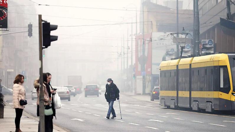 Homem com máscara de proteção contra a poluição atravessa rua envolta em nevoeiro poluente, com o smog a cobrir Sarajevo, Bósnia, quarta-feira, 22 jan. 2025.