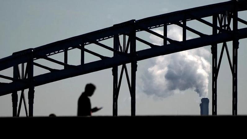 Um homem olha para o telemóvel enquanto atravessa uma ponte, com o fumo de uma incineradora de resíduos ao fundo, nos arredores de Paris, quinta‑feira, 23 de setembro de 2021.
