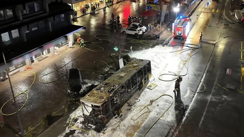 Serviços de emergência acorrem ao esqueleto carbonizado de um autocarro após um incêndio em Kerzers, Suíça, terça-feira, 10 de março de 2026