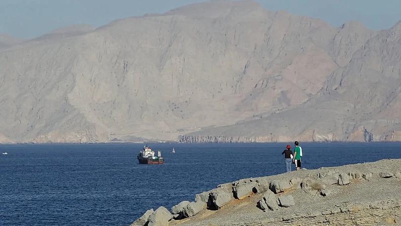 Um casal de turistas contempla as montanhas a sul do Estreito de Ormuz, enquanto navios estão atracados nas águas do Golfo Pérsico, perto da cidade de Khasab, em Omã
