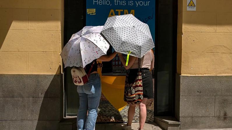 Duas mulheres junto a uma caixa multibanco protegem-se do sol com chapéus-de-chuva durante uma vaga de calor em Madrid, Espanha, domingo, 15 de agosto de 2021