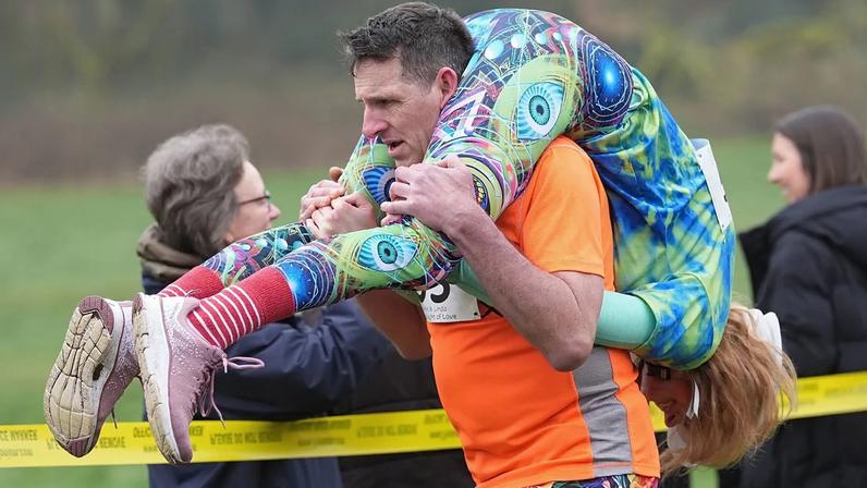Participantes correm na corrida anual britânica de transporte de esposas em Dorking, Inglaterra, domingo, 8 de março de 2026