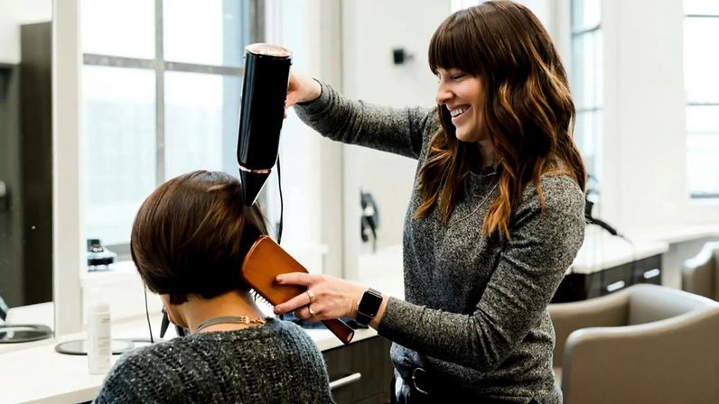 Um cabeleireiro seca o cabelo de uma cliente com o secador.