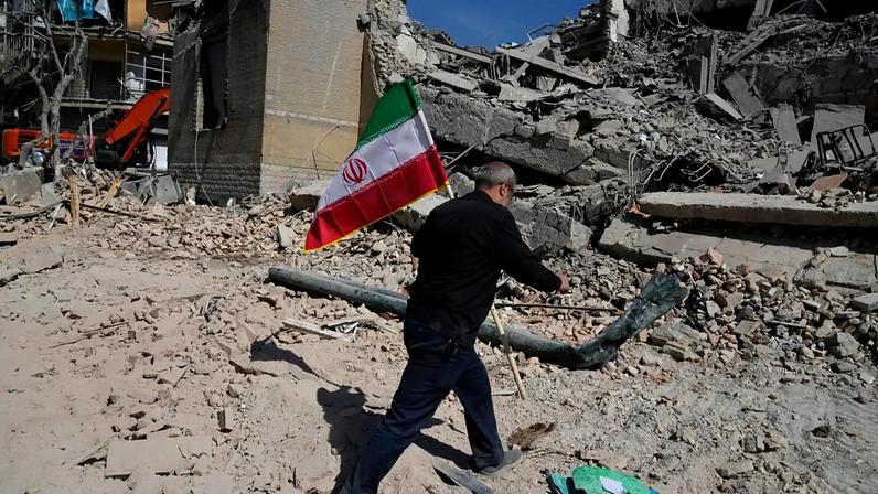 Um homem carrega uma bandeira iraniana para a colocar sobre os escombros de uma instalação policial atingida durante a campanha militar israelo-americana em Teerão, Irão, quarta-feira, 4 de março de 2026.