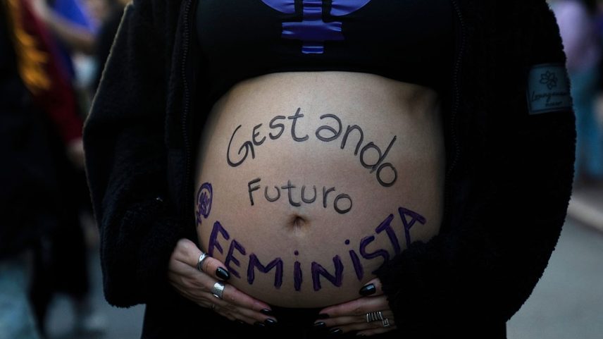 Uma mulher participa numa marcha feminista com a barriga pintada com uma mensagem.