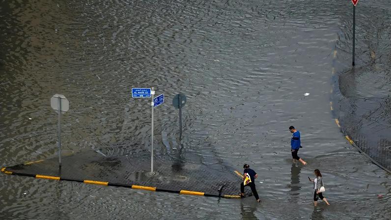 Pendulares avançam por uma rua inundada após forte chuvada em Sharjah, Emirados Árabes Unidos, quarta-feira, 25 de março de 2026.