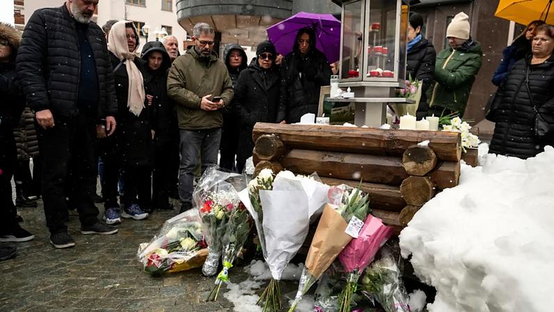 Familiares das vítimas guardam um minuto de silêncio à porta do bar Constellation em Crans-Montana, na Suíça, no sábado, 14 de fevereiro de 2026.