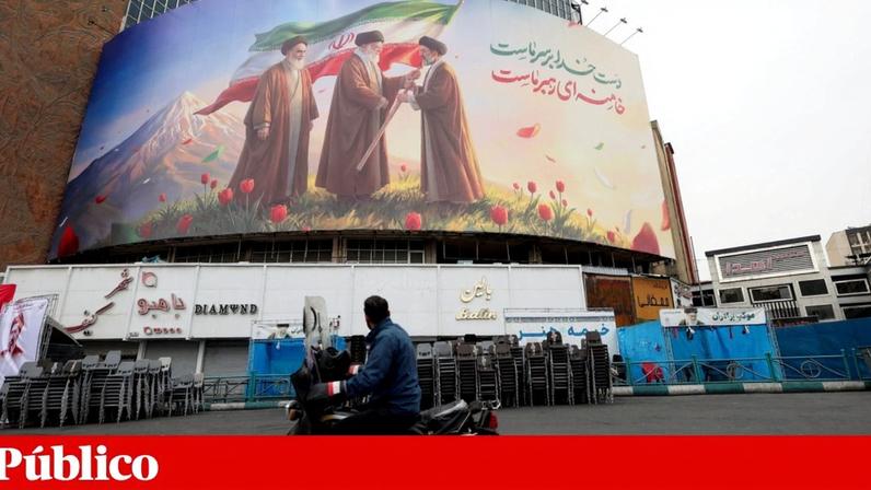 Um homem olha para um cartaz que junta Mojtaba e os anteriores *ayatollah*