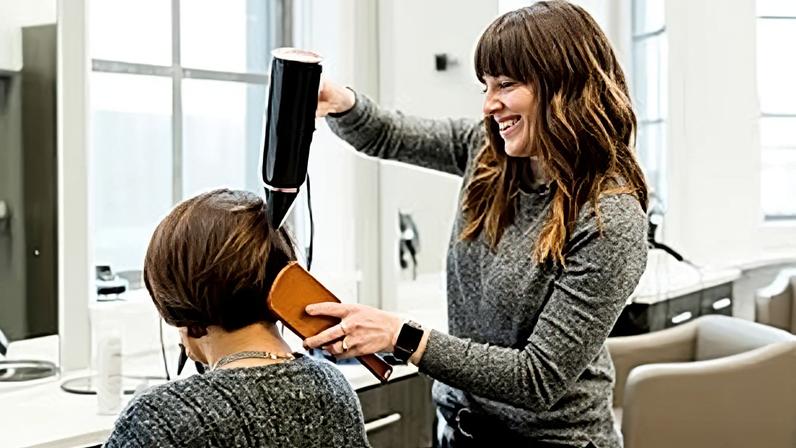 Cabeleireira a secar o cabelo de uma cliente com o secador