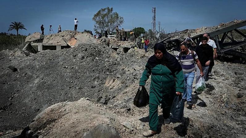 Pessoas atravessam a pé uma cratera na sequência de um ataque aéreo israelita que destruiu a ponte de Qasmiyeh, perto da cidade costeira de Tiro, 16 de abril de 2026