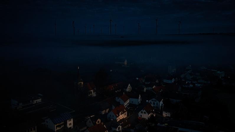 O nevoeiro flutua sobre a aldeia de Stetten, na Alemanha, terça-feira, 19 de março de 2024, com uma central de energia eólica ao fundo.