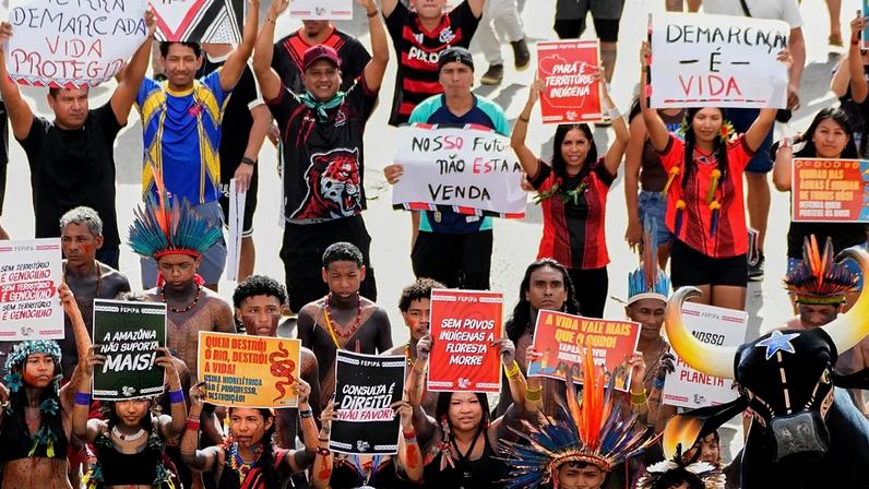 Manifestantes exibem cartazes a exigir a demarcação das suas terras durante uma marcha no Acampamento Terra Livre 2026