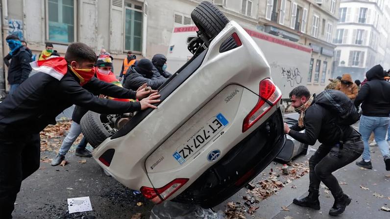 ARQUIVO - Manifestantes viram um carro durante um protesto contra o tiroteio no centro cultural curdo em Paris, 24 de dezembro de 2022.