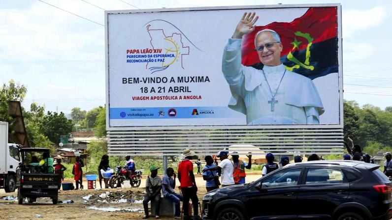 Populares junto de um placar alusivo à visita do Papa Leão XIV em Muxima, no município da Quissama, província de Luanda