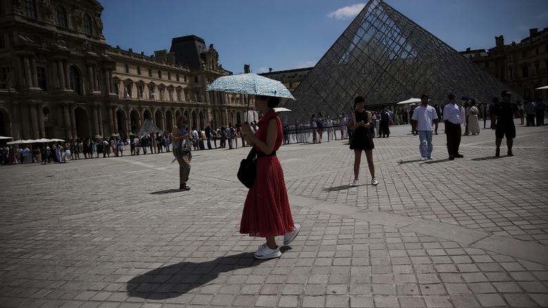 ARQUIVO - Uma mulher segura o guarda-chuva para se proteger do sol no Museu do Louvre, em Paris, numa sexta-feira, 20 de junho de 2025, com 31 ºC