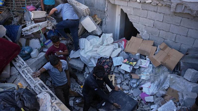 Palestinianos inspecionam os escombros de um edifício destruído num ataque aéreo israelita em Nuseirat, centro da Faixa de Gaza, terça-feira, 26 de maio de 2026