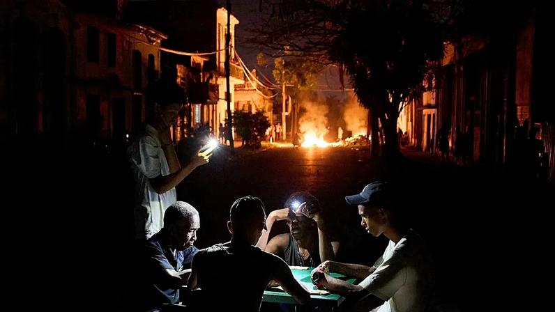 Pessoas iluminam-se com os seus telemóveis enquanto uma fogueira montada por residentes em protesto contra os prolongados cortes de eletricidade arde em Havana, 14 de maio de 2026