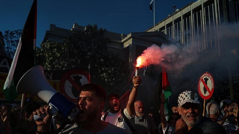 Manifestante ergue um sinal de fumo enquanto outros entoam palavras de ordem pró-palestinianas