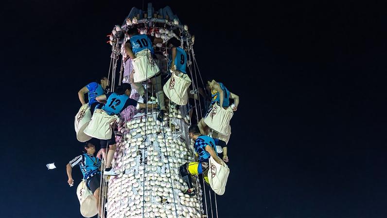 Participantes recolhem pãezinhos de uma torre coberta com pãezinhos de plástico durante o Festival do Pão em Cheung Chau, em Hong Kong, segunda-feira, 25 de maio de 2026