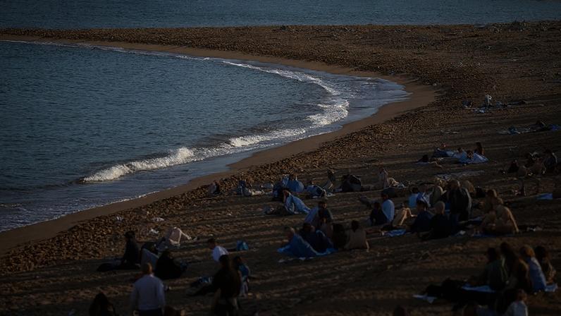 ARQUIVO - Pessoas apanham sol numa praia de Barcelona, Espanha, em 12 de março de 2023.