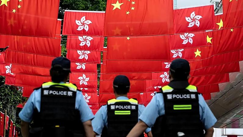 Agentes da polícia passam em frente às bandeiras da China e de Hong Kong, em Hong Kong, a 1 de julho de 2024
