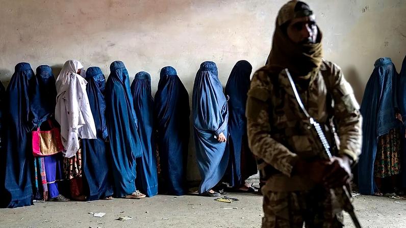 Um combatente talibã monta guarda enquanto mulheres aguardam para receber rações alimentares distribuídas por um grupo de ajuda humanitária