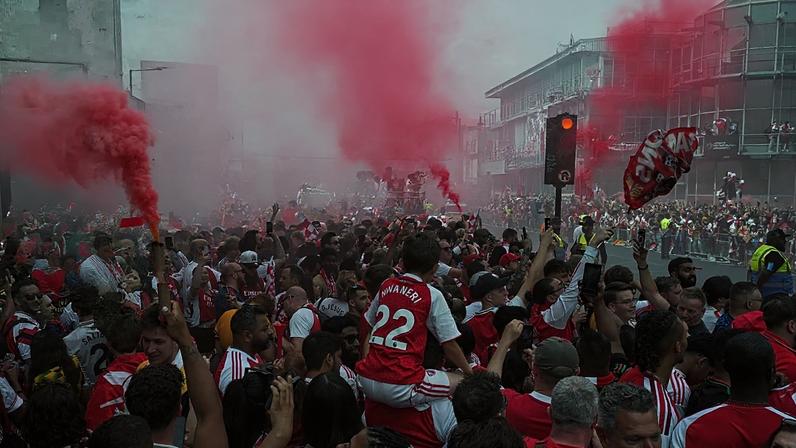 Adeptos do Arsenal agitam bandeiras e acendem tochas enquanto aguardam o desfile do autocarro descoberto após o título da Premier League, em Londres, 31 de maio de 2026.