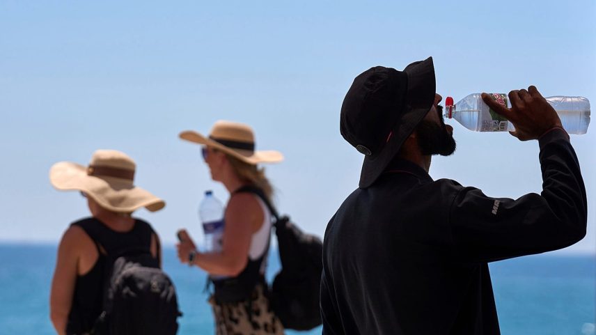 Turista bebe água de uma garrafa na praia de Barcelona