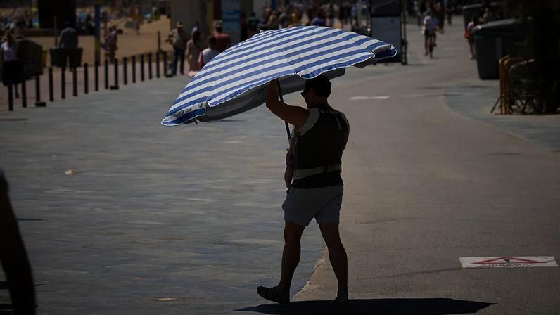 Um homem segura um guarda-chuva enquanto caminha perto de uma praia em Barcelona, Espanha, na quarta-feira, 27 de maio de 2026.