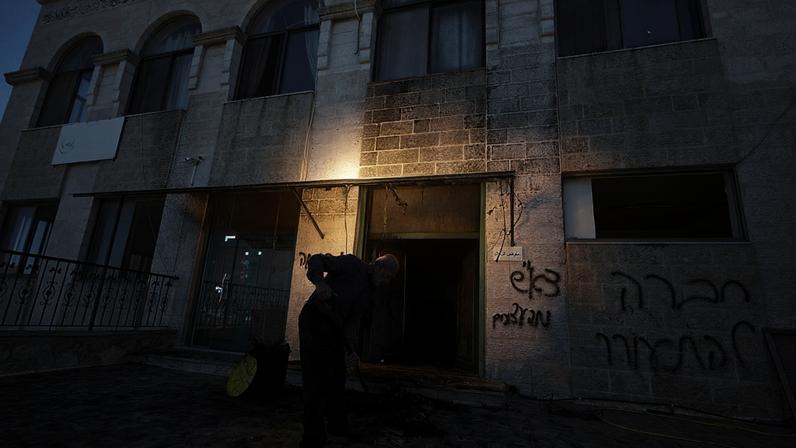 Homem remove escombros de uma mesquita na Cisjordânia, danificada num ataque noturno, com graffiti em hebraico a apelar à "vingança" numa parede