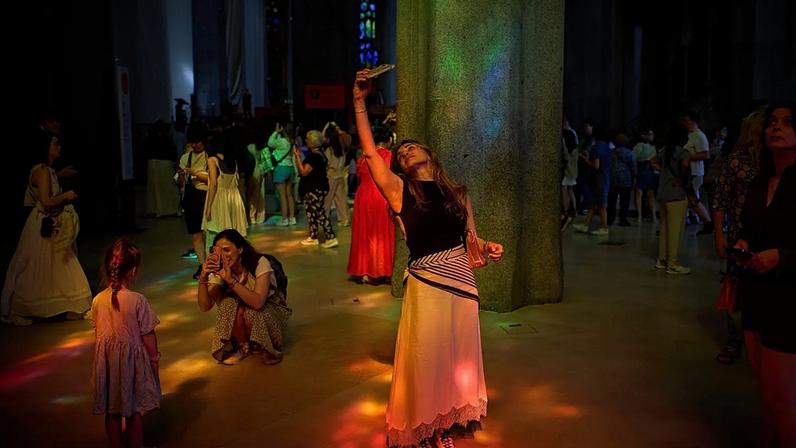 Uma turista fotografa o interior da Sagrada Família enquanto a luz dos vitrais ilumina o templo, terça-feira, 26 de maio de 2026, em Barcelona