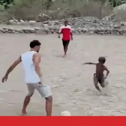 Avó descalça joga à bola com crianças num campo de terra batida em Cabo Verde