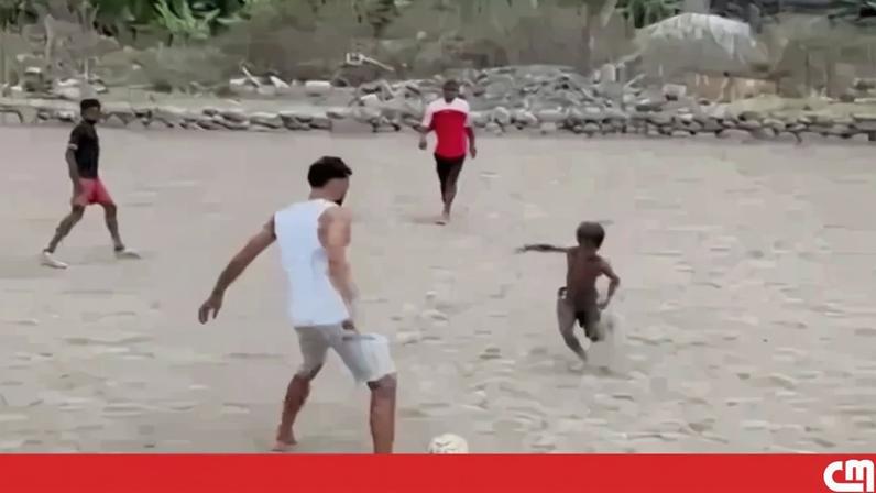 Avó descalça joga à bola com crianças num campo de terra batida em Cabo Verde