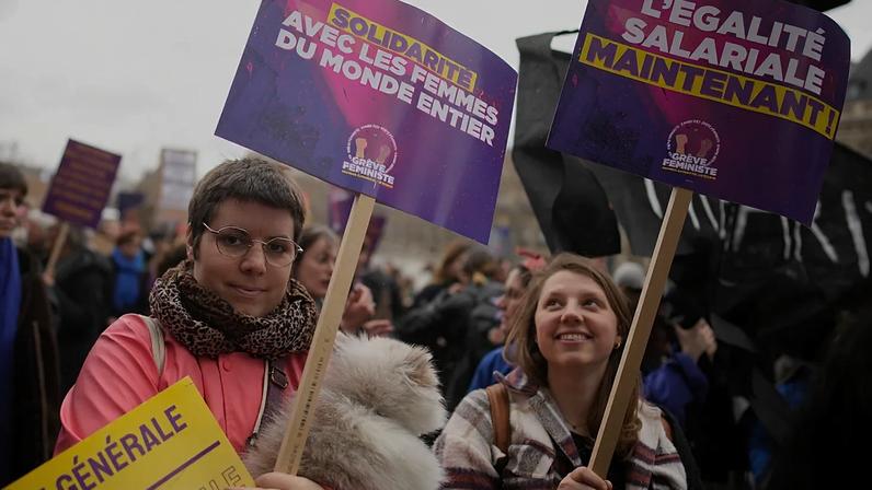 Mulheres manifestam-se com cartazes onde se lê «Igualdade salarial já», à direita, e «Solidariedade com as mulheres de todo o mundo», numa marcha do Dia Internacional da Mulher